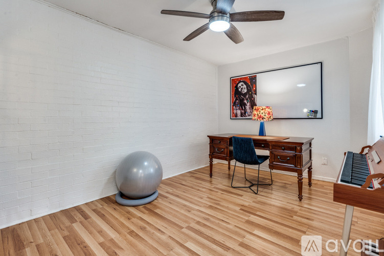 A room with a wooden floor, a desk with a chair, a ball, and a ceiling fan.
