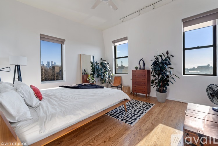 A bedroom with a large bed, a wooden floor, and a view of the city through the windows.