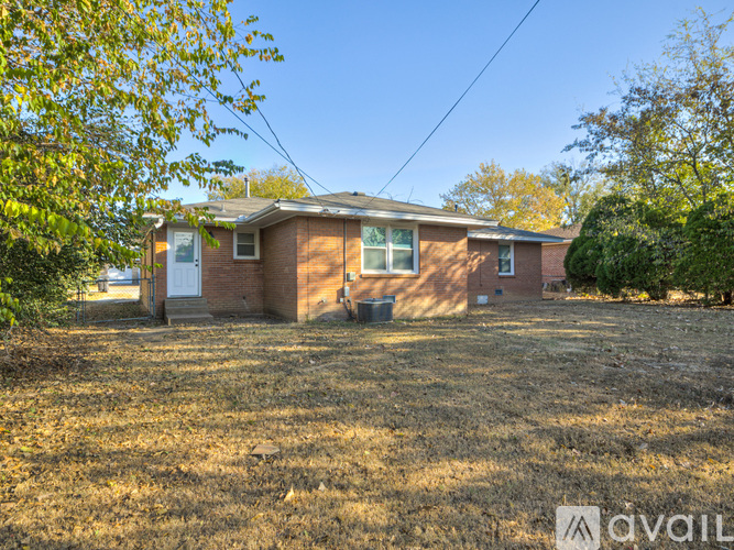 A house with a brown brick exterior and a white door is surrounded by a grassy area with trees.