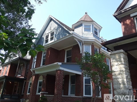 A red brick house with a white balcony and a blue roof.