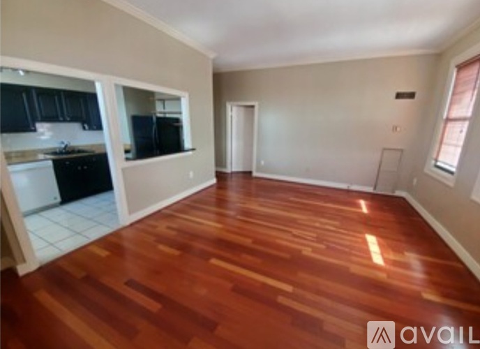 A room with wooden flooring and a kitchen area in the background.
