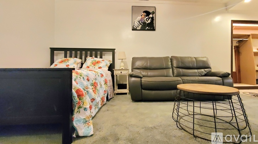 A black leather sofa sits in a room with a bed and a small table.