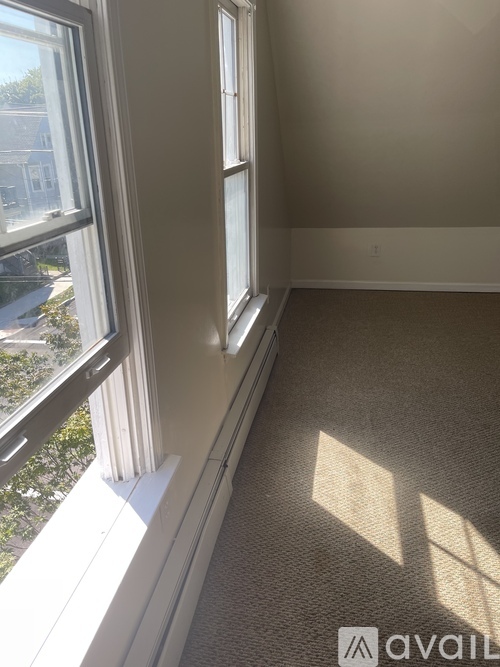 A room with a carpeted floor and a window letting in sunlight.
