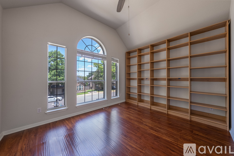 A room with wooden floors and a large window with a view of a street and buildings outside.