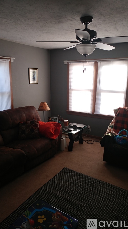 A living room with a brown couch, a small table, and a ceiling fan.