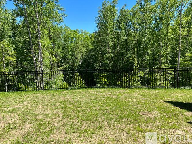 A grassy field with a fence and trees in the background.