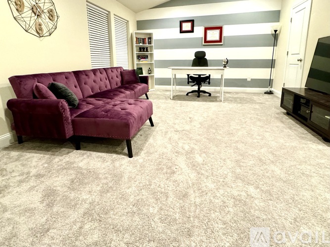 A living room with a purple couch and a grey carpet.