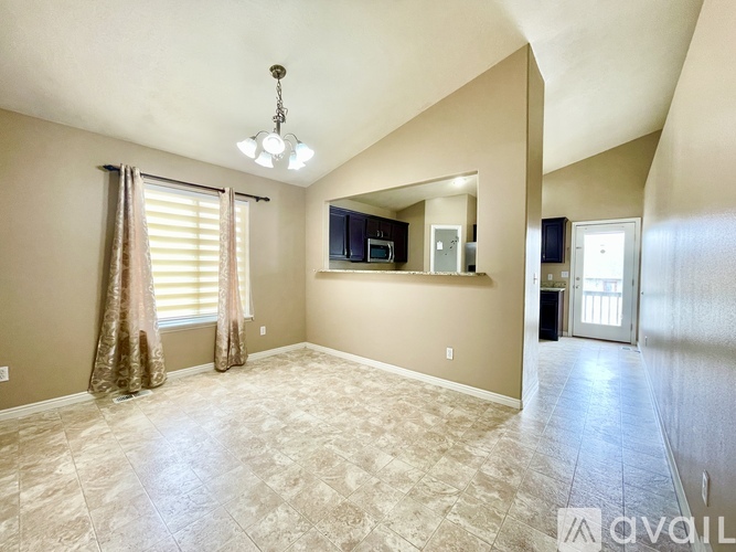 A spacious living room with a television, a window with curtains, and a chandelier.