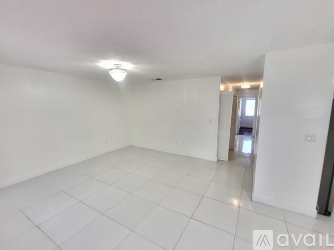 A spacious room with white tiled flooring and a single light fixture on the ceiling.