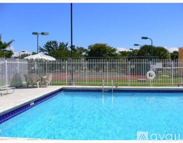 A pool surrounded by a fence with chairs and umbrellas in the background.