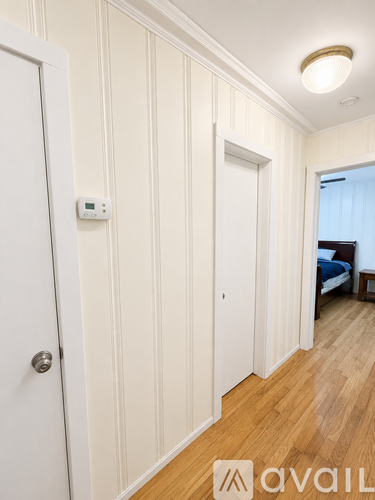 A hallway with a door on the left and a bedroom at the end.