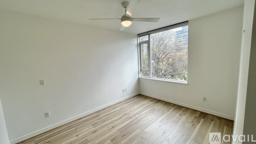A room with a ceiling fan and a window with a view of trees outside.