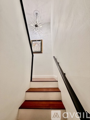 A staircase with a wooden handrail and a chandelier hanging from the ceiling.