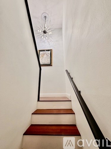 A staircase with a wooden handrail and a chandelier hanging from the ceiling.