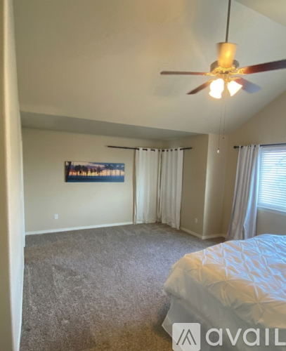 A bedroom with a bed, a ceiling fan, and a window with curtains.