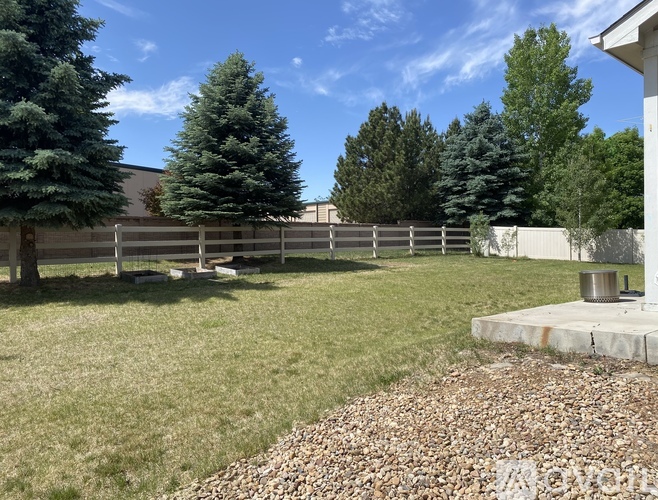 A backyard with a fence, trees, and a gravel area.