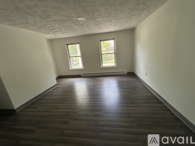 A room with wooden flooring and two windows.