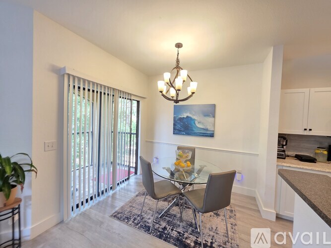 A dining room with a glass table and chairs, a chandelier, and a painting on the wall.