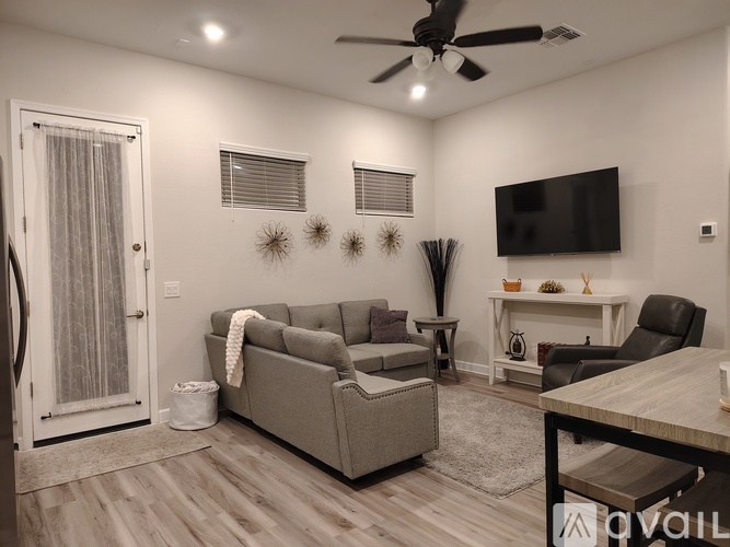 A living room with a grey couch, a black chair, a white table, and a television mounted on the wall.