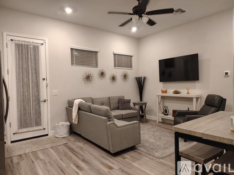 A living room with a grey couch, a black chair, a white table, and a television mounted on the wall.