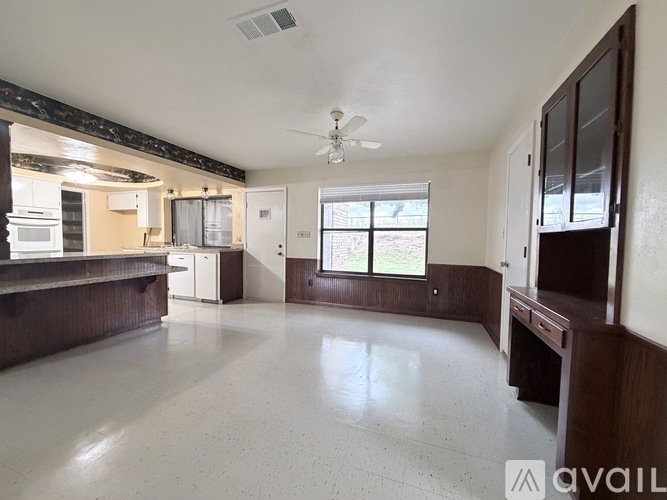A room with wooden flooring and a kitchen area in the background.