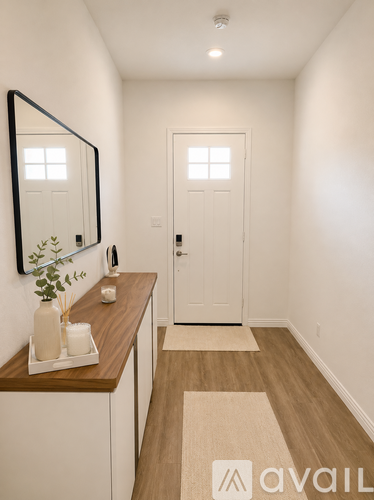 A hallway with a mirror, a door, and a tray with candles and a plant on a wooden counter.