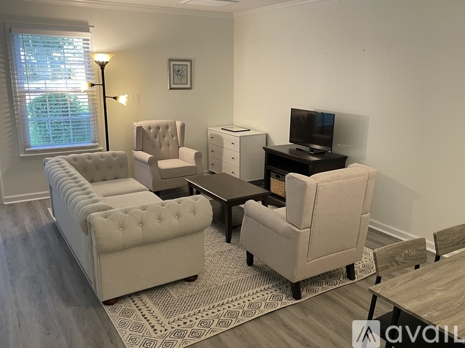 A living room with a white couch, a white chair, a white ottoman, a black coffee table, a white TV, and a white rug.