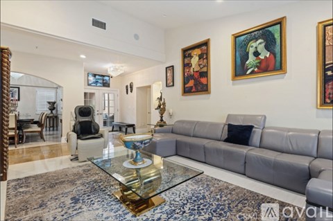 A living room with a grey couch, a glass coffee table, and a painting on the wall.