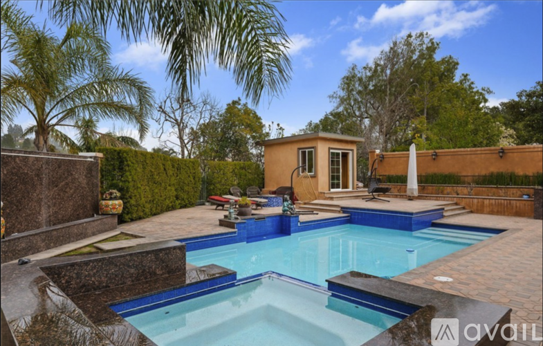 A swimming pool in a backyard with a small house and palm trees.