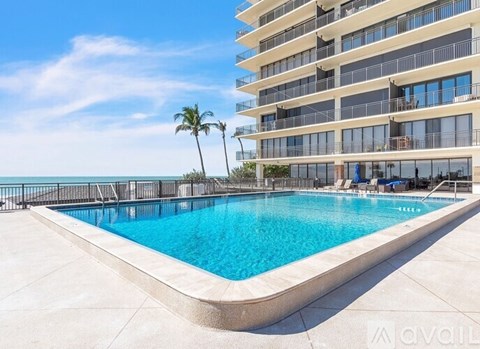 A swimming pool in front of a multi-story building with balconies and palm trees.