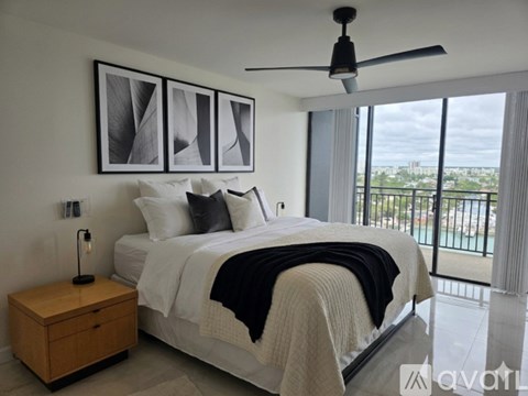 A bedroom with a large bed, a ceiling fan, and a view of the city.