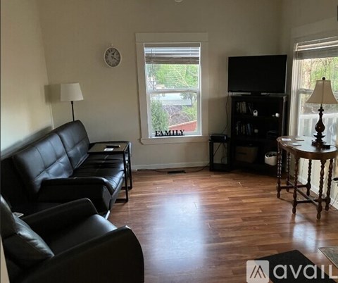 A living room with a black leather couch and a wooden floor.