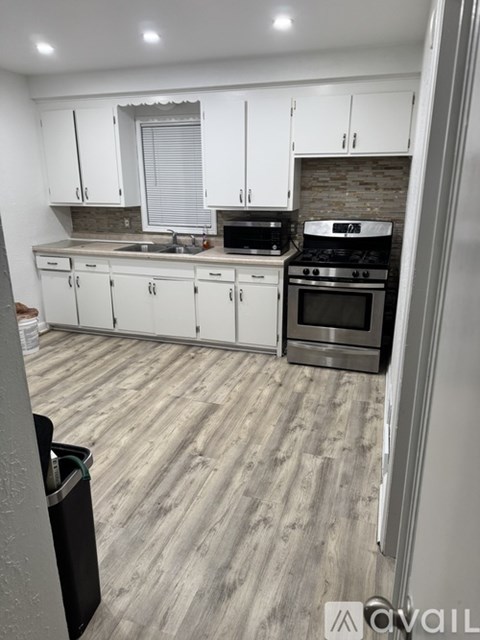 A kitchen with white cabinets and a black trash can.