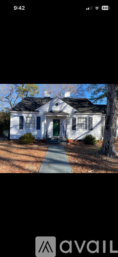 A white house with a green door and a tree in front.