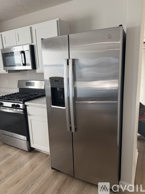 A stainless steel refrigerator stands in a kitchen with a stove and microwave in the background.