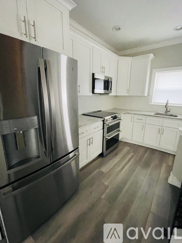 A modern kitchen with a stainless steel refrigerator and wooden flooring.