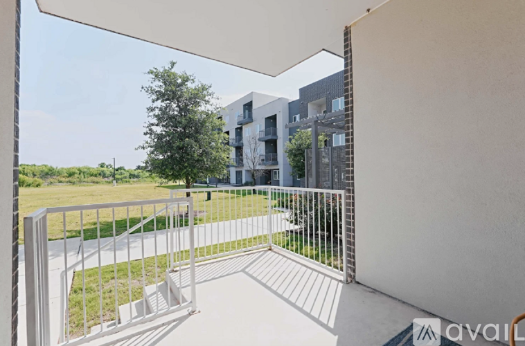 A balcony with a white railing overlooks a grassy area and modern buildings.
