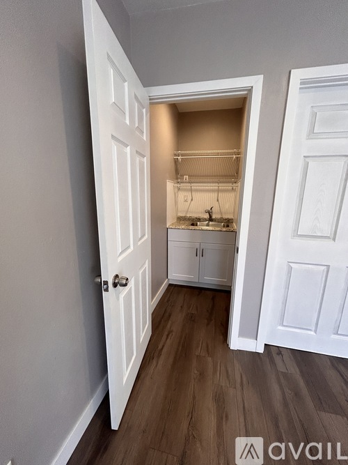 A white door is open to a kitchen with wood floors.