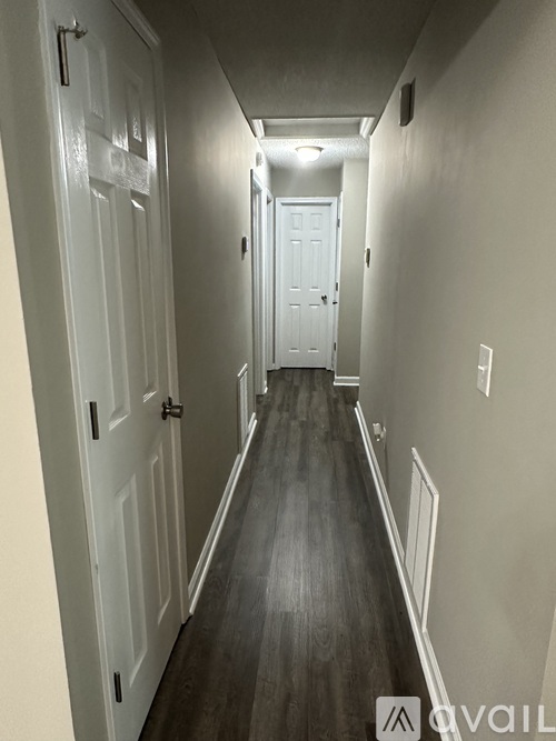 A long hallway with white doors on the left and a white door at the end.