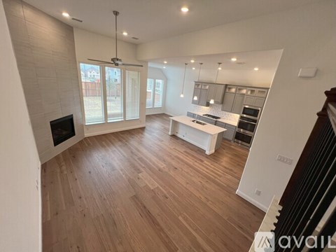 A spacious living room with wooden flooring and a kitchen area in the background.