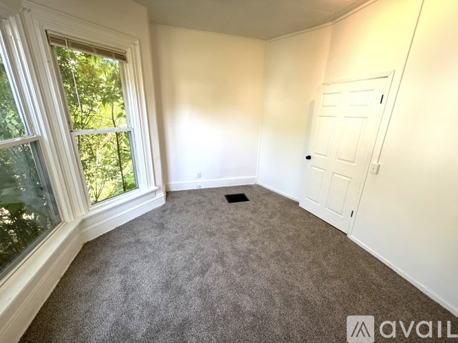 A room with a carpeted floor, a door, and a window with a view of trees.