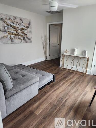 A grey couch is in front of a white wall with a painting on it.