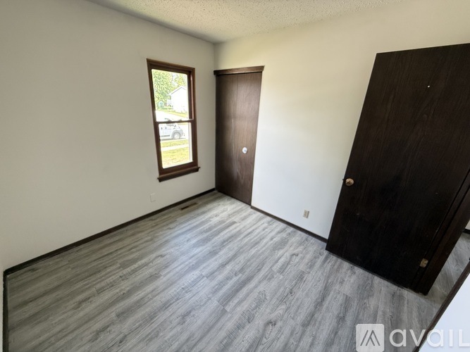 A room with a wooden floor and a window showing a view of a house and trees outside.