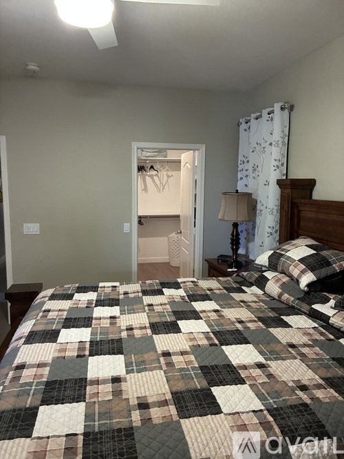 A bedroom with a bed covered in a plaid comforter and a lamp on a side table.