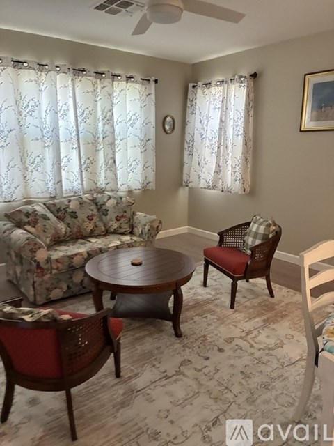 A living room with a floral sofa, a round table, and a chair with a red cushion.