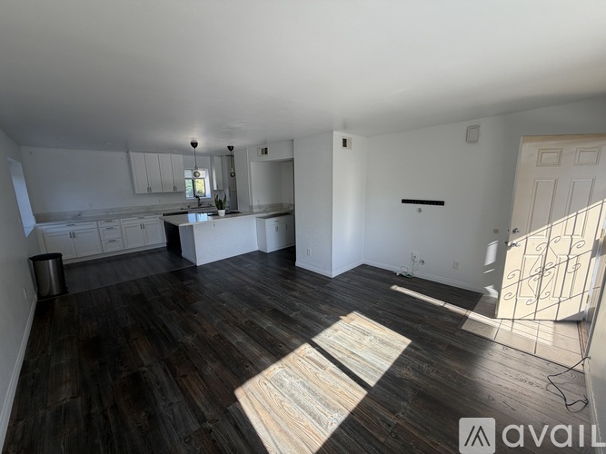 A spacious room with dark wood flooring and white walls.
