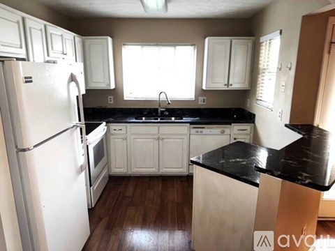 A kitchen with white cabinets and black countertops.