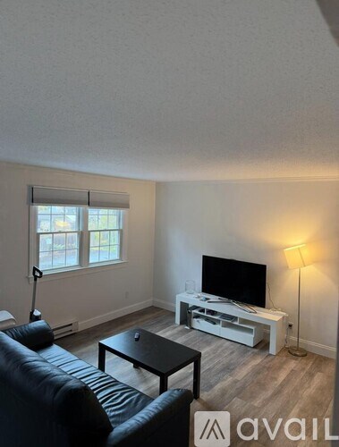 A living room with a black leather couch, a wooden coffee table, a flat screen TV, and a floor lamp.