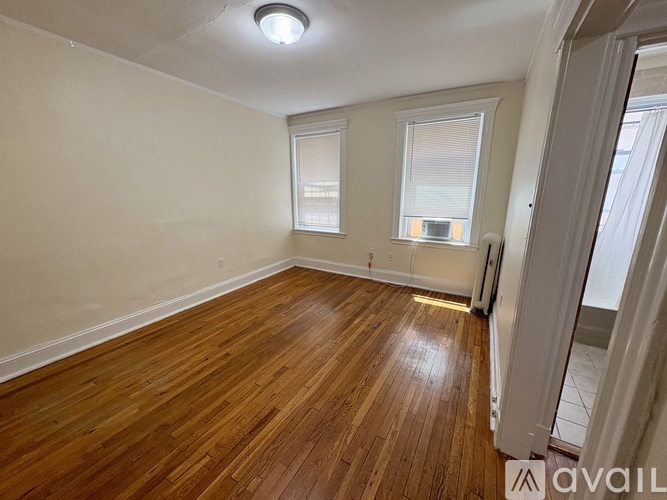 A room with wooden flooring and two windows.
