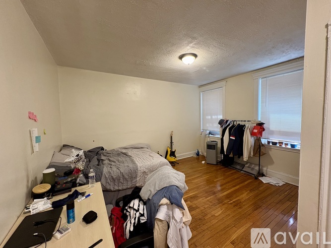 A bedroom with a bed, desk, and clothes hanging up.